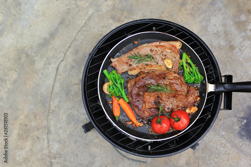 Raw beef steak with vegetables in frying pan on tiled floor background, food meat or barbecue