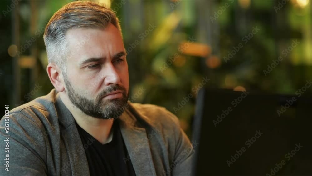 Young bearded Hipster Man, Entrepreneur Sits on Couch at Coffee Table, Uses Laptop With Blank Screen. On Table Notebook and Cup of Coffee. Online Marketing, Education, E-learning, Startup. Young bearded Hipster Man, Entrepreneur Sits on Couch at Coffee Table, Uses Laptop With Blank Screen. On Table Notebook and Cup of Coffee. Online Marketing, Education, E-learning, Startup.