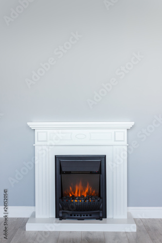 White wooden decorative electric fireplace with a beautiful burning flame. Interior photo on gray background. Place for a simple text.