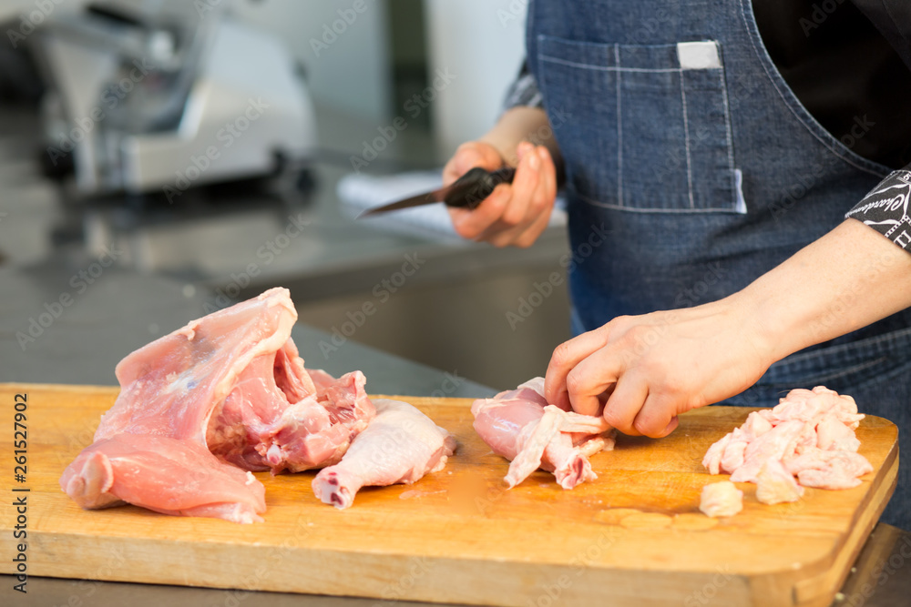 A chef  in uniform cuts raw chicken. Cook's hand with a knife close-up on the background of the kitchen.