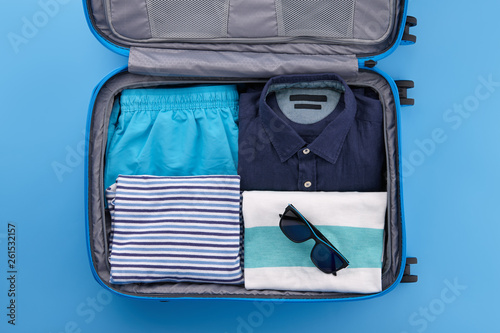 Travel suitcase with clothes on blue background