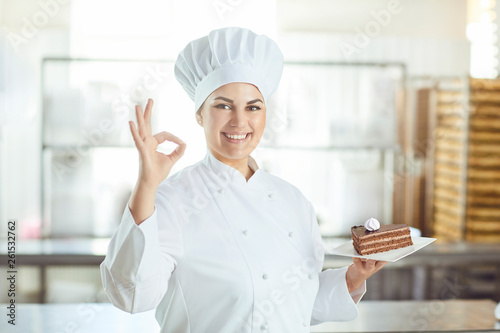 Confectioner is holding a cake in her hand in the bakery.
