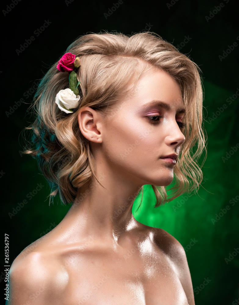 Beautiful young blonde girl with naked shoulders, flowers braided into her hair and oily body poses on a dark green gradient background. Clean, healthy skin. Nude make-up. Close up Beautiful young blonde girl with naked shoulders, flowers braided into her hair and oily body poses on a dark green gradient background. Clean, healthy skin. Nude make-up. Close up