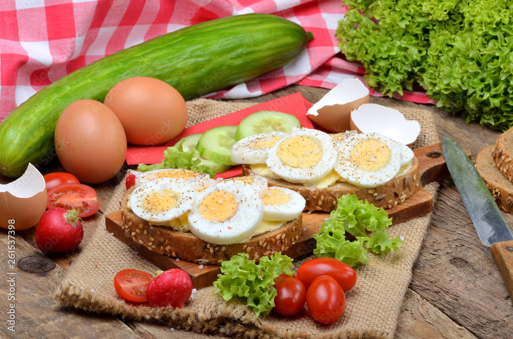 Wholemeal bread with butter, hard-boiled eggs, fresh radishes, tomatoes, salad and cucumbers in background Wholemeal bread with butter, hard-boiled eggs, fresh radishes, tomatoes, salad and cucumbers in background