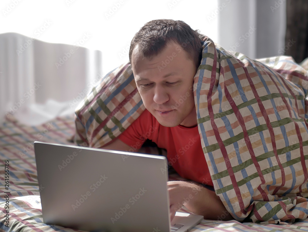 Concept the rest. Young man lying on the bed and typing on a laptop Concept the rest. Young man lying on the bed and typing on a laptop