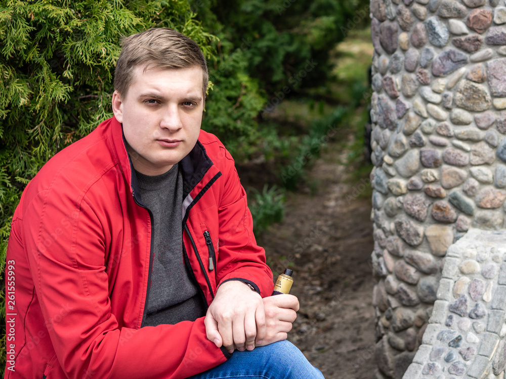 A young guy in a red jacket smokes an electronic cigarette A young guy in a red jacket smokes an electronic cigarette