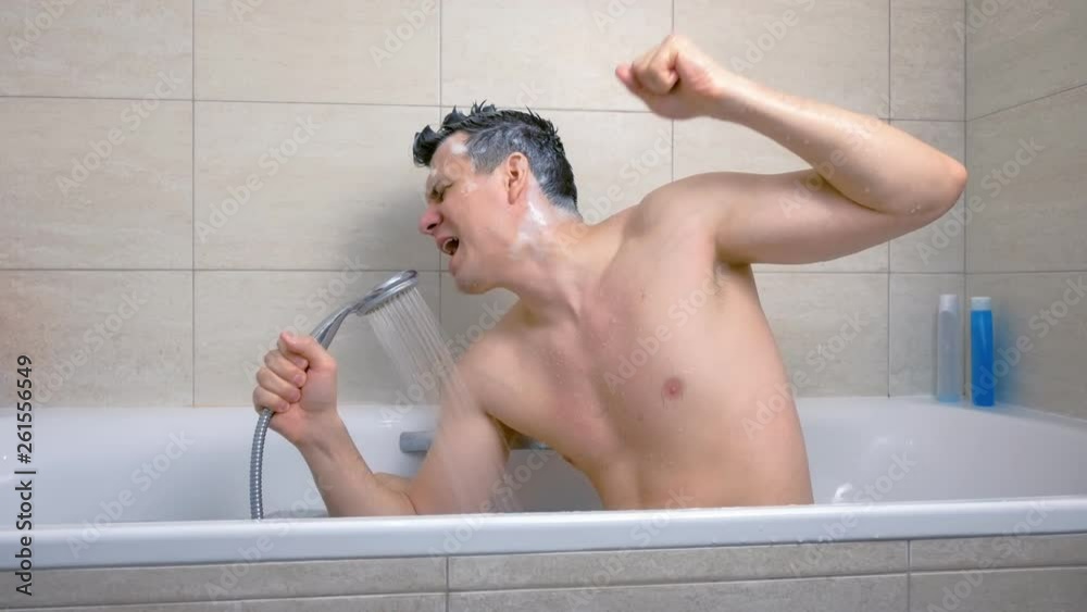 Man with Mohawk shampoo hairs is singing with enthusiasm while he is washing in bathtub. Side view.