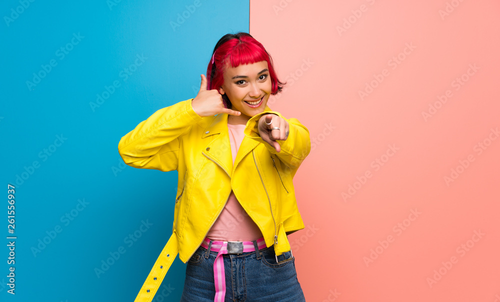Young woman with yellow jacket making phone gesture and pointing front Young woman with yellow jacket making phone gesture and pointing front
