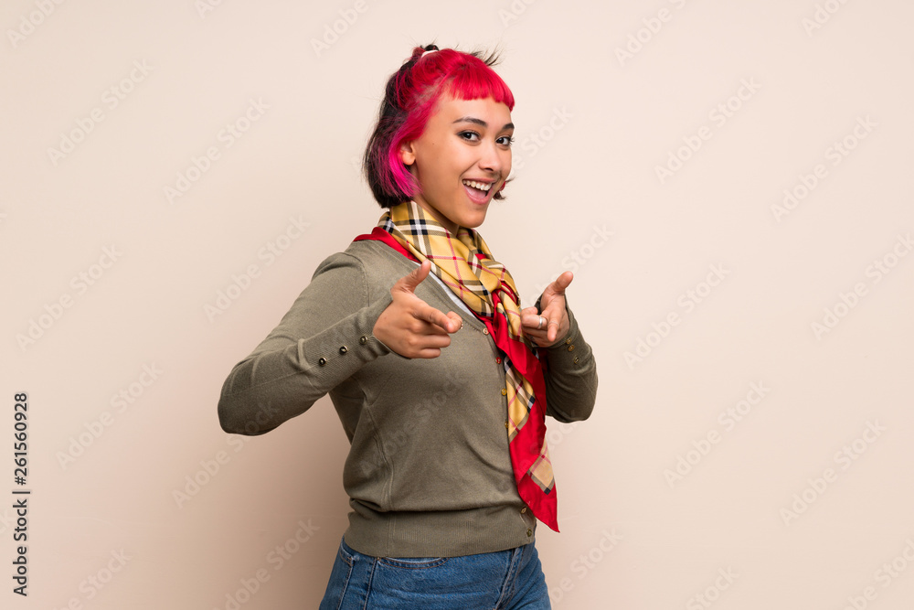 Young woman with pink hair over yellow wall pointing to the front and smiling