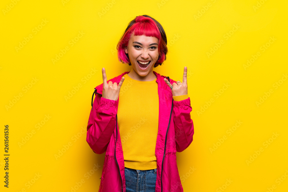 Young woman with pink hair over yellow wall making rock gesture Young woman with pink hair over yellow wall making rock gesture