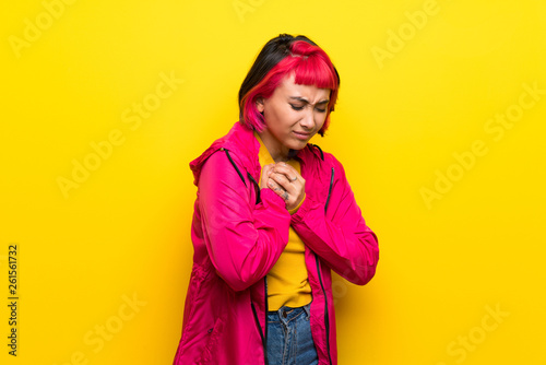 Young woman with pink hair over yellow wall having a pain in the heart © luismolinero