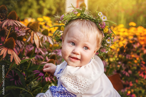 Baby girl in a wreath and Ukrainian embroidered shirt, near the flower beds in the summer Park, Ukrainian child.