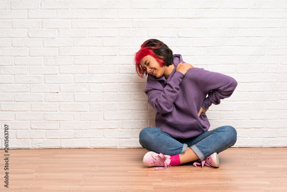Young woman with pink hair sitting on the floor suffering from pain in shoulder for having made an effort Young woman with pink hair sitting on the floor suffering from pain in shoulder for having made an effort
