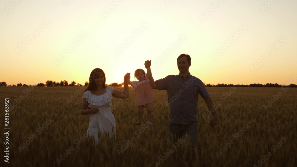 happy daughter with her mom and dad are walking across field of ripe wheat, baby is crumpling. An infant with parents playing and smiling in field with wheat. concept of happy family and childhood