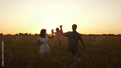 happy daughter with her mom and dad are walking across field of ripe wheat, baby is crumpling. An infant with parents playing and smiling in field with wheat. concept of happy family and childhood © zoteva87