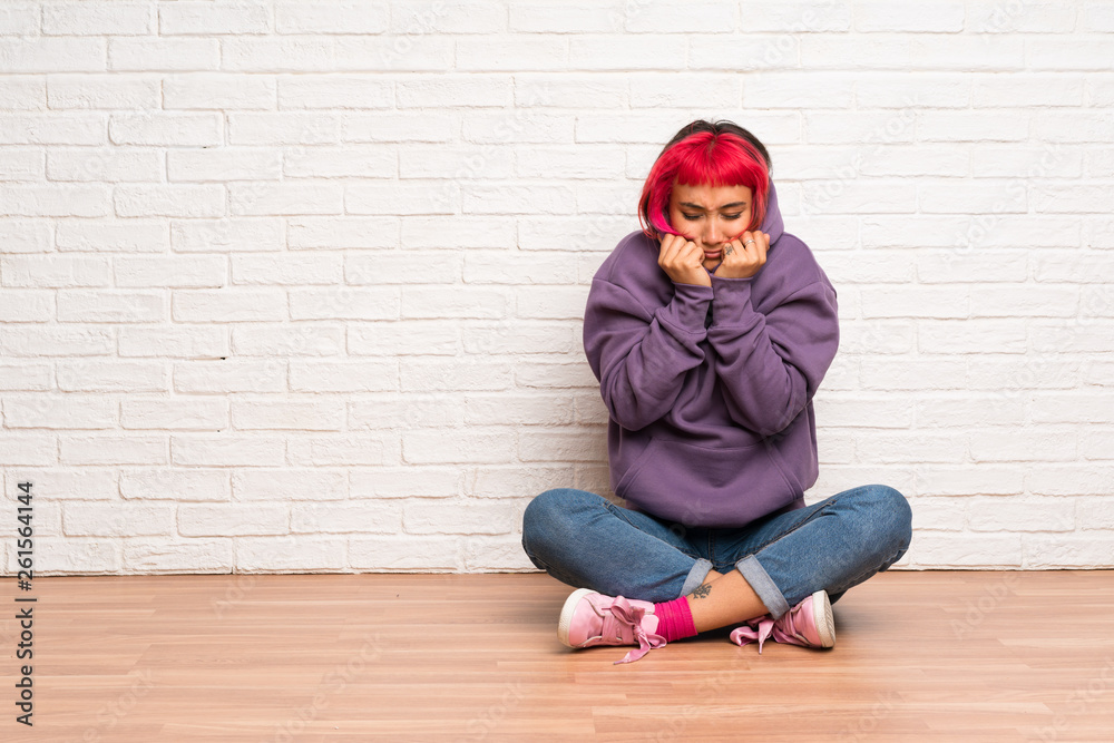 Young woman with pink hair sitting on the floor freezing Young woman with pink hair sitting on the floor freezing