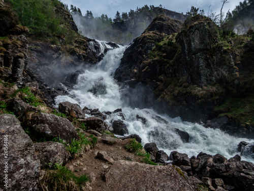 Upper parts of Langfossen waterfall at its splendid. Vast and tall waterfall  flowing around the rocks and in between the trees. Immense power of the nature. The water falls down a towering mountain