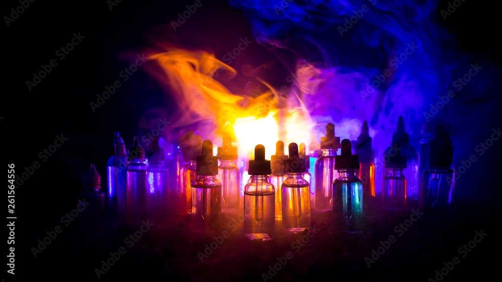 Obraz premium Vape concept. Smoke clouds and vape liquid bottles on dark background. Light effects. Useful as background or electronic cigarette advertisement.
