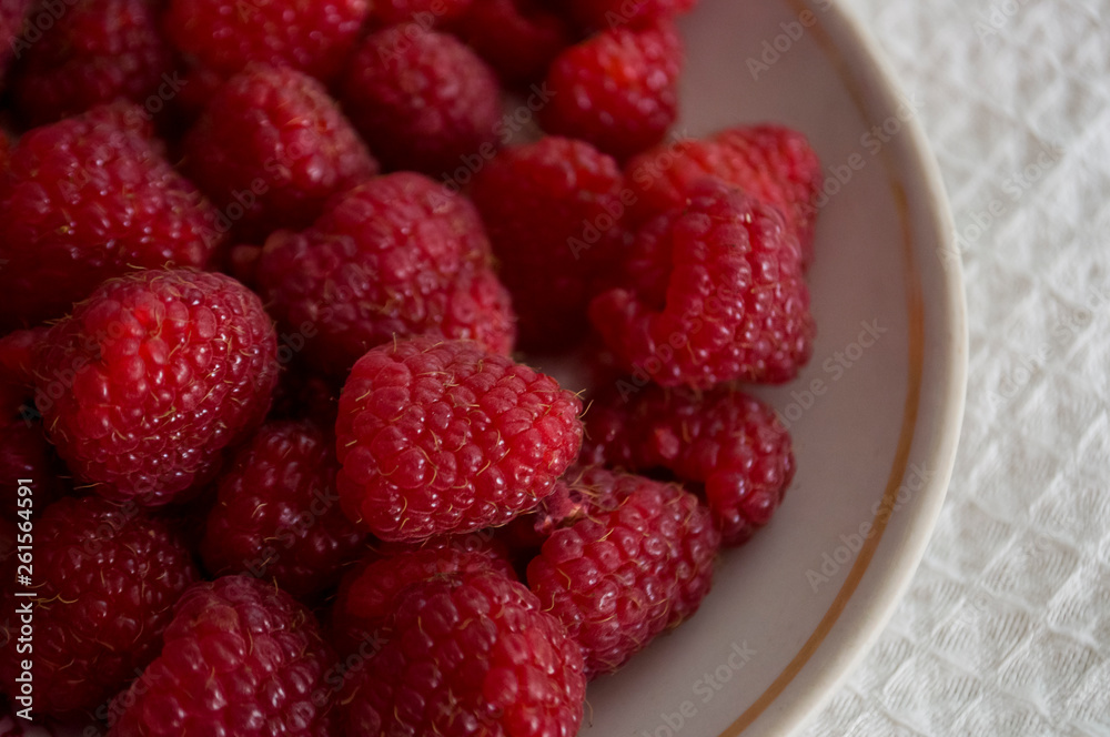 Big ripe raspberries are laying on the  table covered with white tablecloth