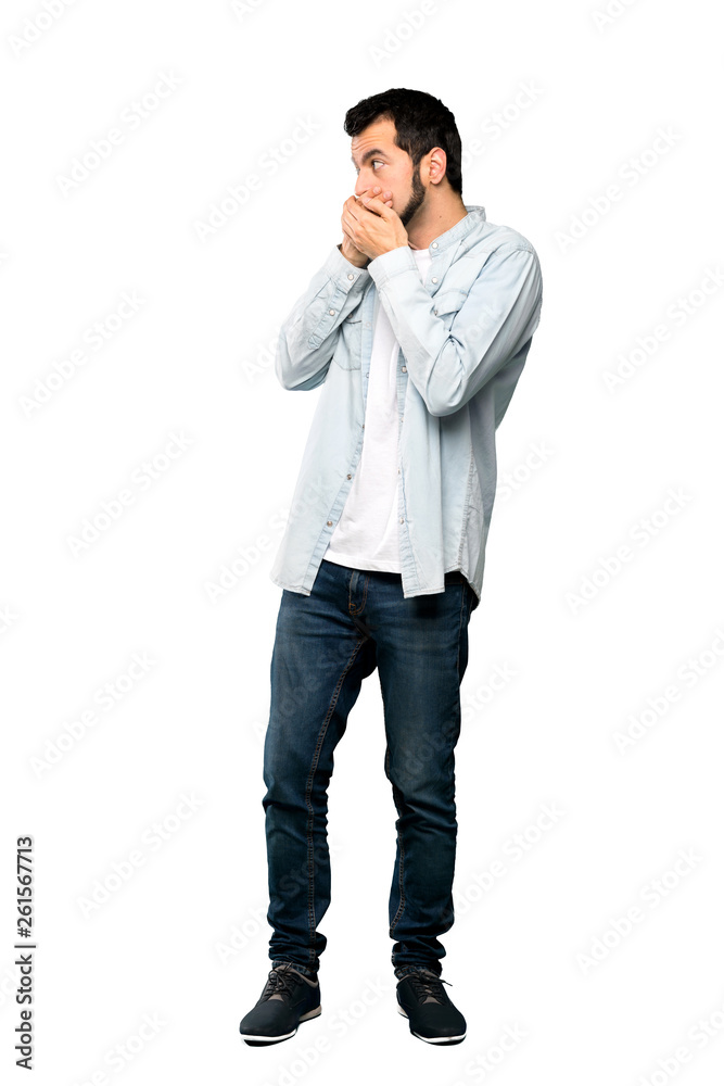 Full-length shot of Handsome man with beard covering mouth and looking to the side over isolated white background Full-length shot of Handsome man with beard covering mouth and looking to the side over isolated white background