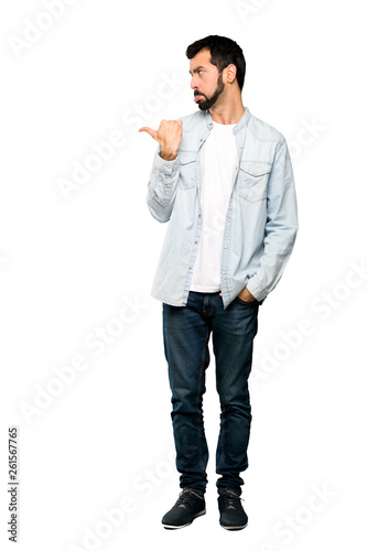 Full-length shot of Handsome man with beard unhappy and pointing to the side over isolated white background