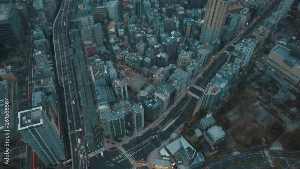 Aerial drone panning directly above the bustling city of Tokyo, Japan full of roads, cars, buildings, offices and skyscrapers on an overcast cloudy day