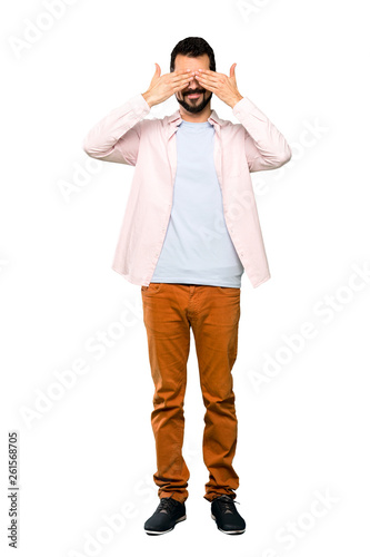 Full-length shot of Handsome man with beard covering eyes by hands over isolated white background