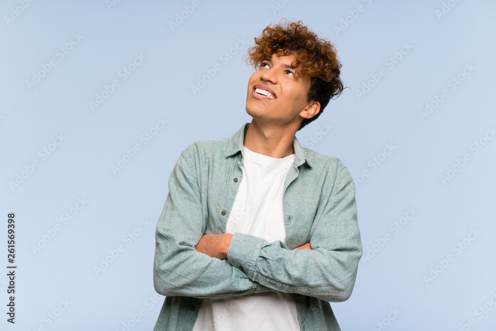 Young african american man over isolated blue wall looking up while smiling Young african american man over isolated blue wall looking up while smiling