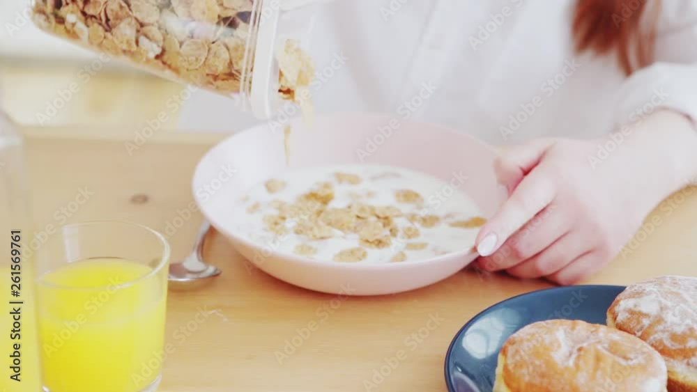 Close-up shot of unrecognizable woman pouring cereals into bowl with milk in slow motion
