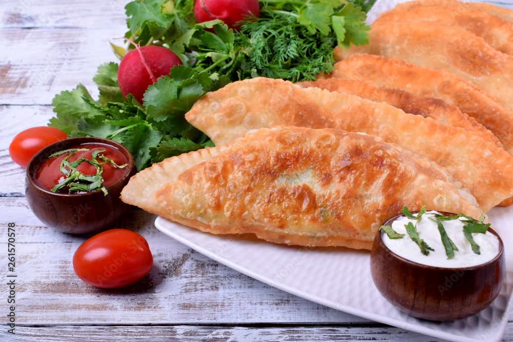 Golden Chebureki on a white plate. Sauces, vegetables and greenery around Golden Chebureki on a white plate. Sauces, vegetables and greenery around