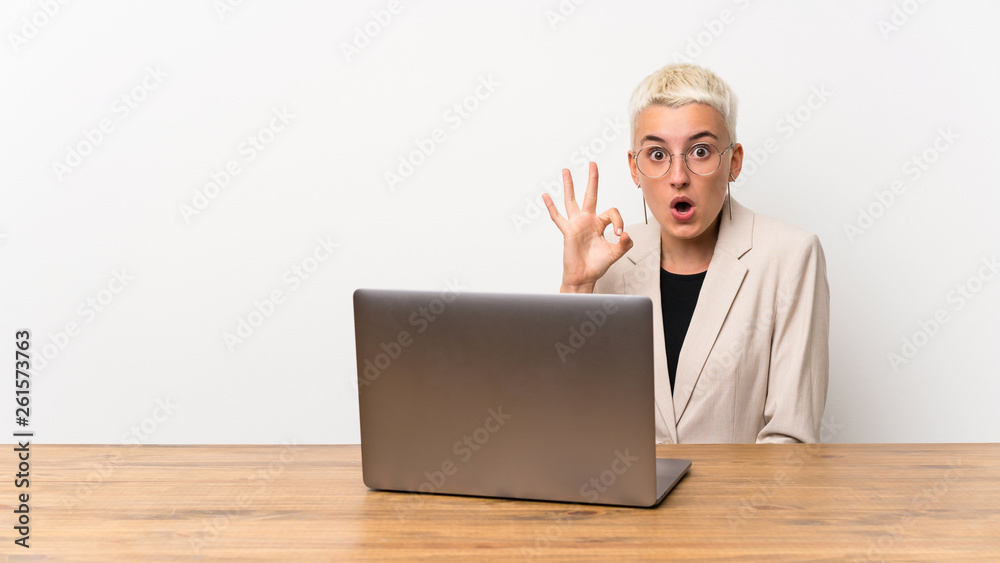 Teenager girl with short hair with a laptop surprised and showing ok sign Teenager girl with short hair with a laptop surprised and showing ok sign