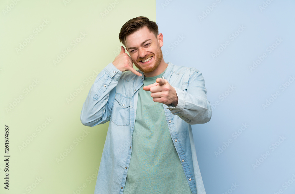 Redhead man over colorful background making phone gesture and pointing front Redhead man over colorful background making phone gesture and pointing front