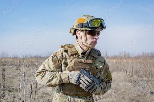 Male soldier in nato uniform with hand gun outoors in the field