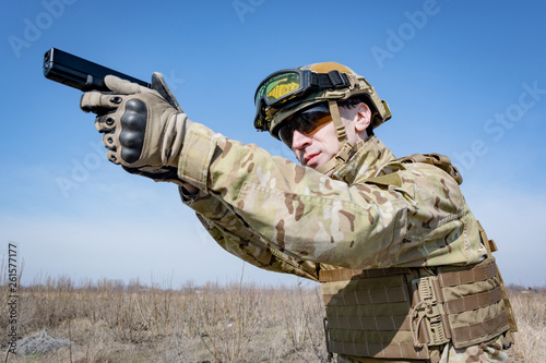 Male soldier in nato uniform with hand gun outoors in the field