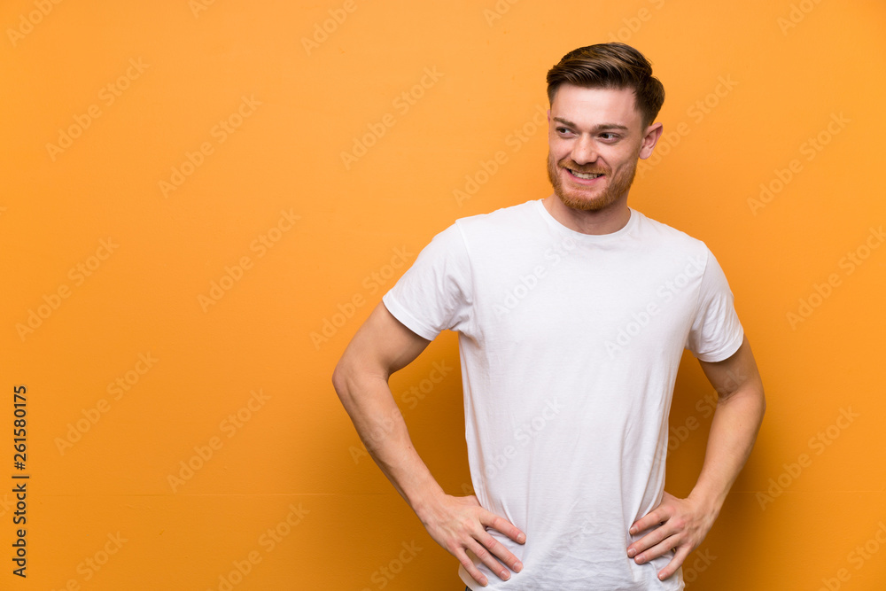 Redhead man over brown wall posing with arms at hip and smiling Redhead man over brown wall posing with arms at hip and smiling