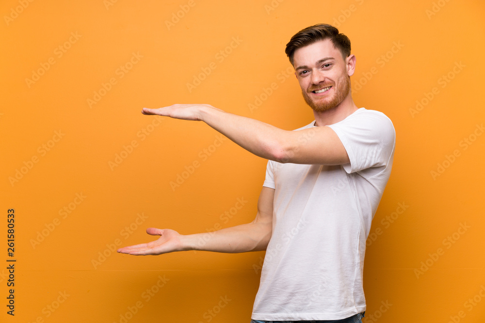 Redhead man over brown wall holding copyspace to insert an ad