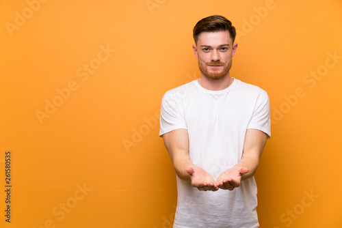Redhead man over brown wall holding copyspace imaginary on the palm to insert an ad