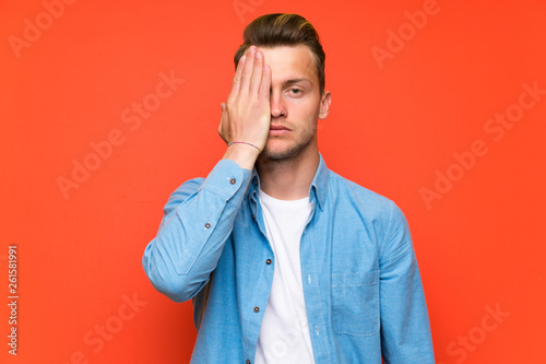Blonde handsome man over isolated wall covering a eye by hand