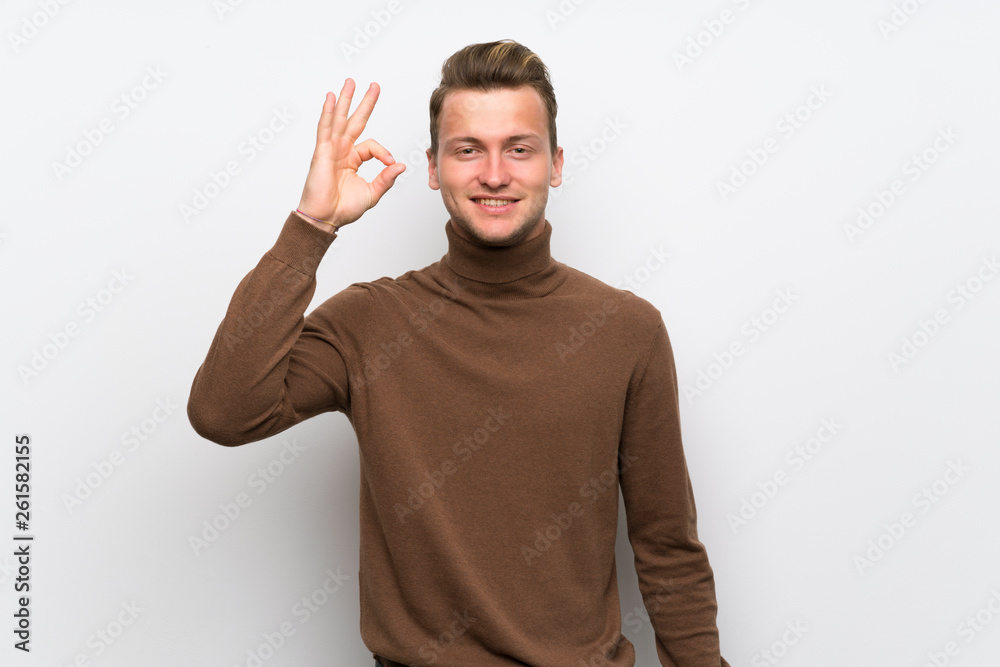 Fototapeta premium Blonde man over isolated white wall showing an ok sign with fingers