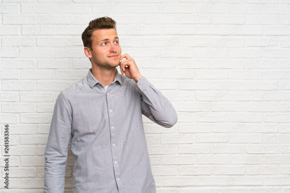 Blonde man over white brick wall thinking an idea while looking up Blonde man over white brick wall thinking an idea while looking up