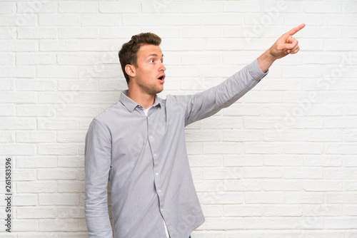 Blonde man over white brick wall pointing away