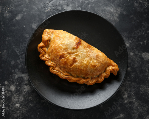 Leinwand Poster Traditional Cornish pasty filled with beef meat, potato and vegetables on black