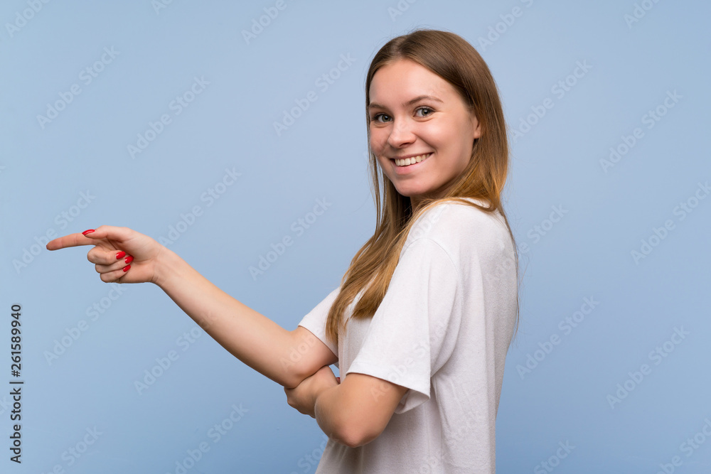 Young woman over blue wall pointing finger to the side in lateral position Young woman over blue wall pointing finger to the side in lateral position
