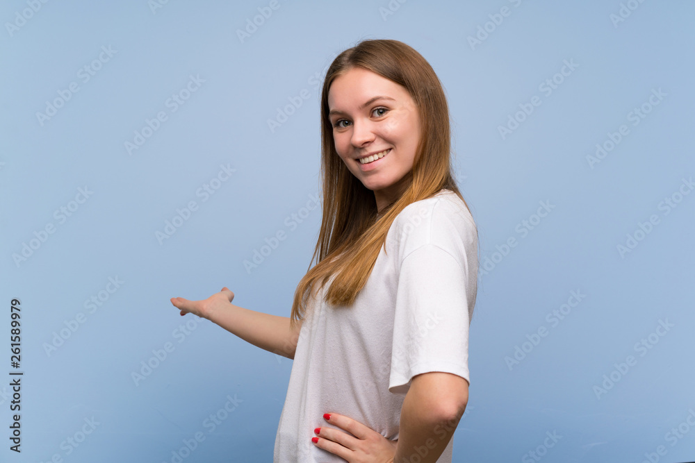 Young woman over blue wall pointing back and presenting a product Young woman over blue wall pointing back and presenting a product