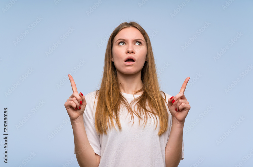 Young woman over blue wall surprised and pointing up Young woman over blue wall surprised and pointing up