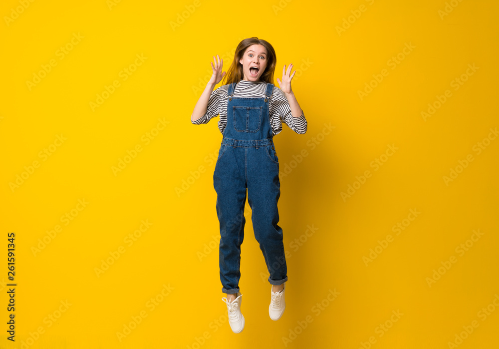 Young girl with overalls jumping over isolated yellow background Young girl with overalls jumping over isolated yellow background