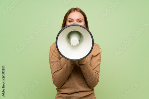 Young woman with turtleneck sweater shouting through a megaphone