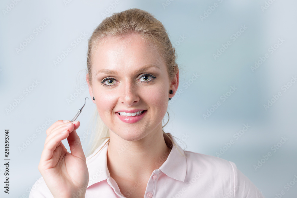 young female dentist with dental tool in her hand in front of clinic room young female dentist with dental tool in her hand in front of clinic room