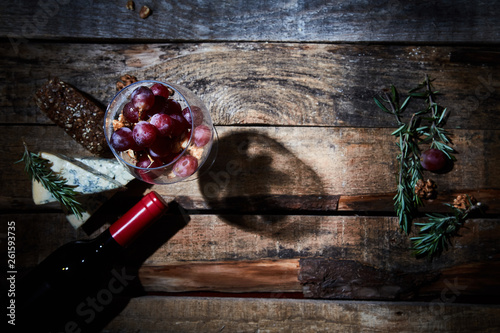 Gourmet composition of wineglass with grapes and walnuts on wood table with cheese and bottle of red wine photo