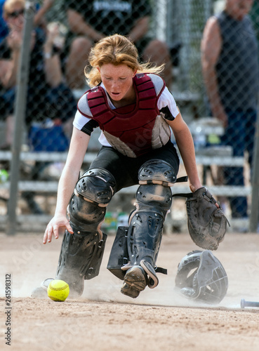 Bilde på lerret Skilled softbaall catcher with red hair and protective gear scrambling for the loose ball on the field